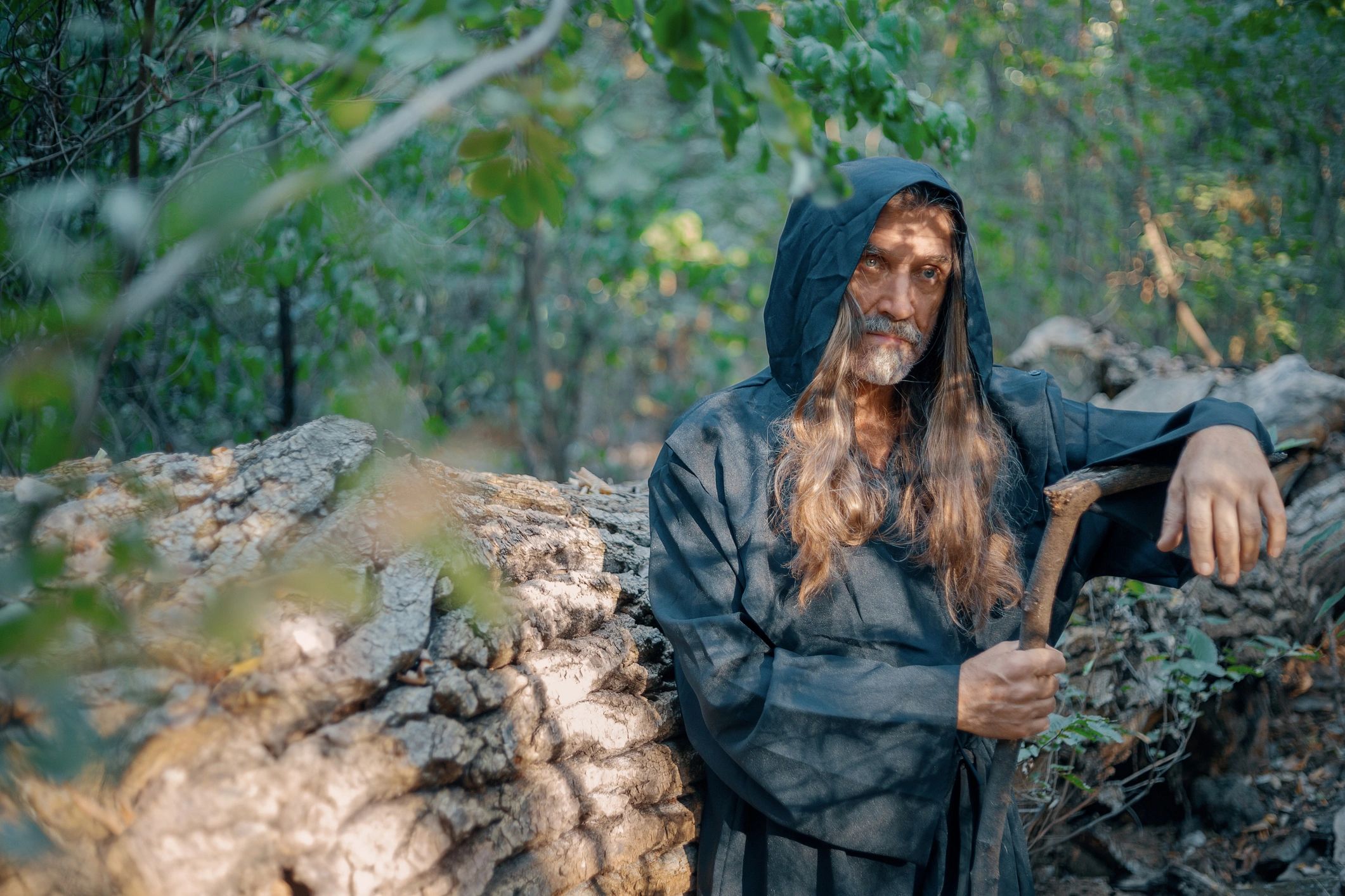 Wizard in fantasy robe holding wooden staff in forest